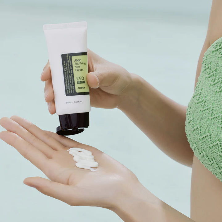 COSRX Aloe Soothing Sun Cream being squeezed onto a person’s hand, showing creamy white texture.