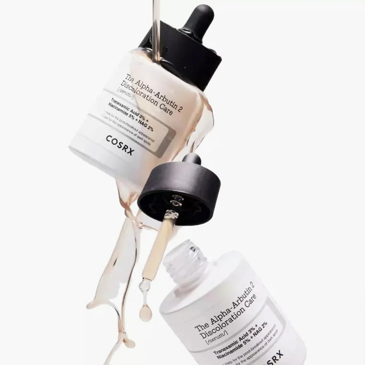 Two COSRX Alpha-Arbutin 2 Discoloration Care Serum bottles with droppers dispensing the serum, highlighting its lightweight liquid texture.