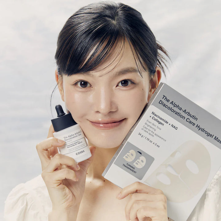 Smiling woman holding COSRX Alpha-Arbutin 2 Discoloration Care Serum and Hydrogel Mask, showcasing skincare routine.