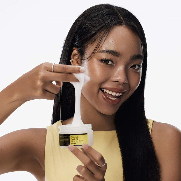 Woman showing stretchy texture of COSRX Advanced Snail 92 All in One Cream from the jar.